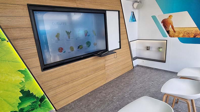 Modern ICL exhibition space featuring a large interactive screen displaying crop information, white chairs for visitors, and colorful agricultural graphics on the walls, creating a clean and engaging learning environment.