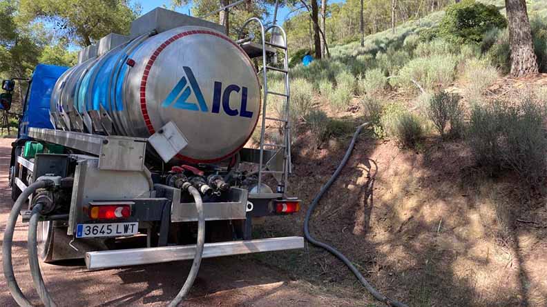 An ICL water truck parked on a forest path in Sierra Espuña, with hoses extended to deliver water to newly planted saplings on the hillside. The scene shows reforestation efforts amid trees and natural vegetation.