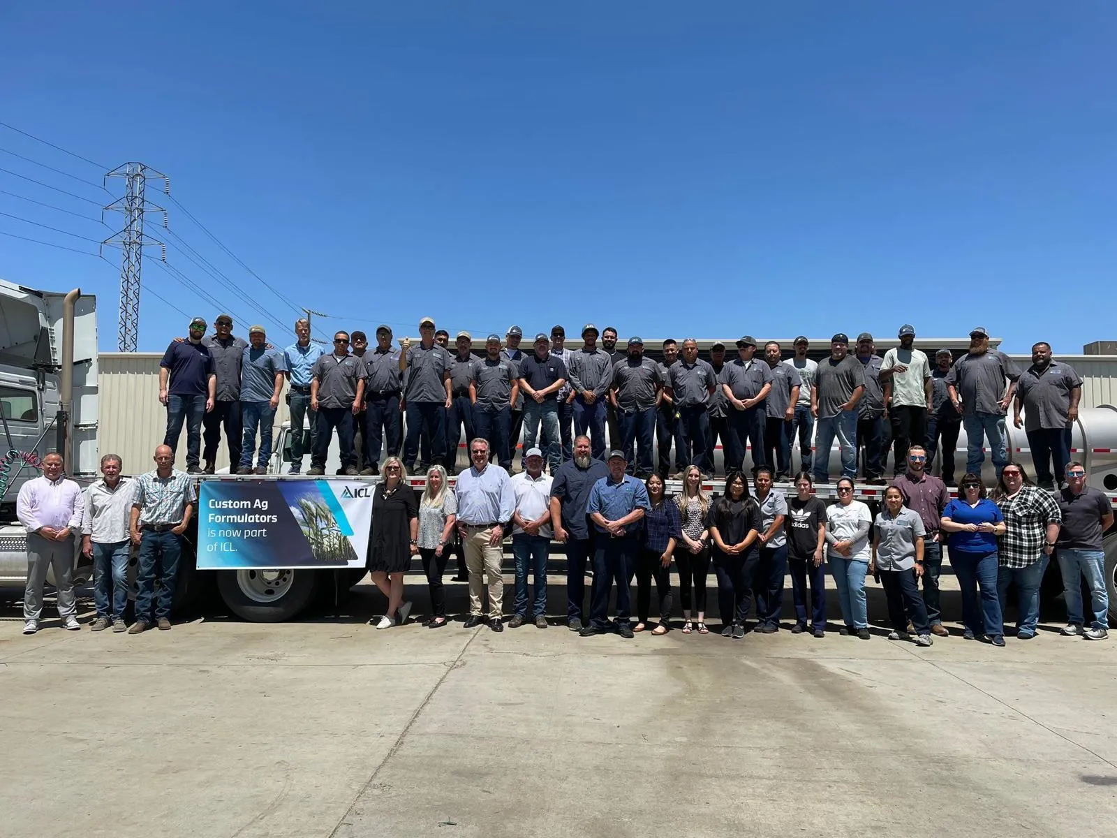 Group photo of Custom Ag Formulators team and ICL employees standing together outdoors in front of company trucks, celebrating Custom Ag Formulators joining ICL.