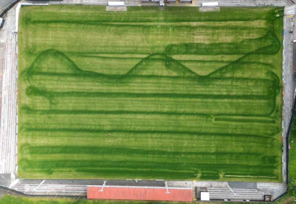 Errori di applicazione del concime con il carrello applicatore su campo di calcio Striature scure e storte su campo di calcio dovute a errori di spargimento del concime a causa di un uso sbagliato dello spandiconcime. Direzione e andatura sono errate